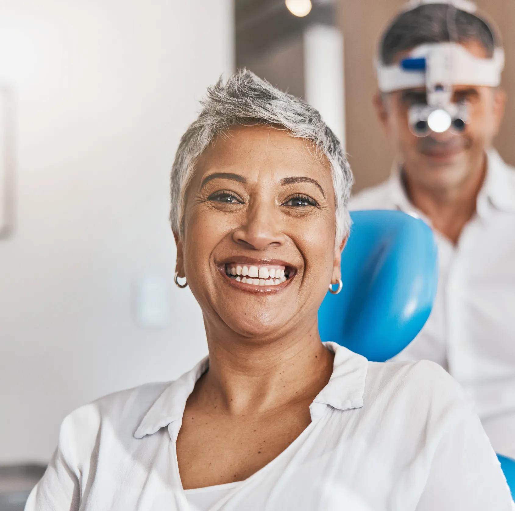 A woman wearing a dark jacket smiles while standing in a hallway with her arms crossed.