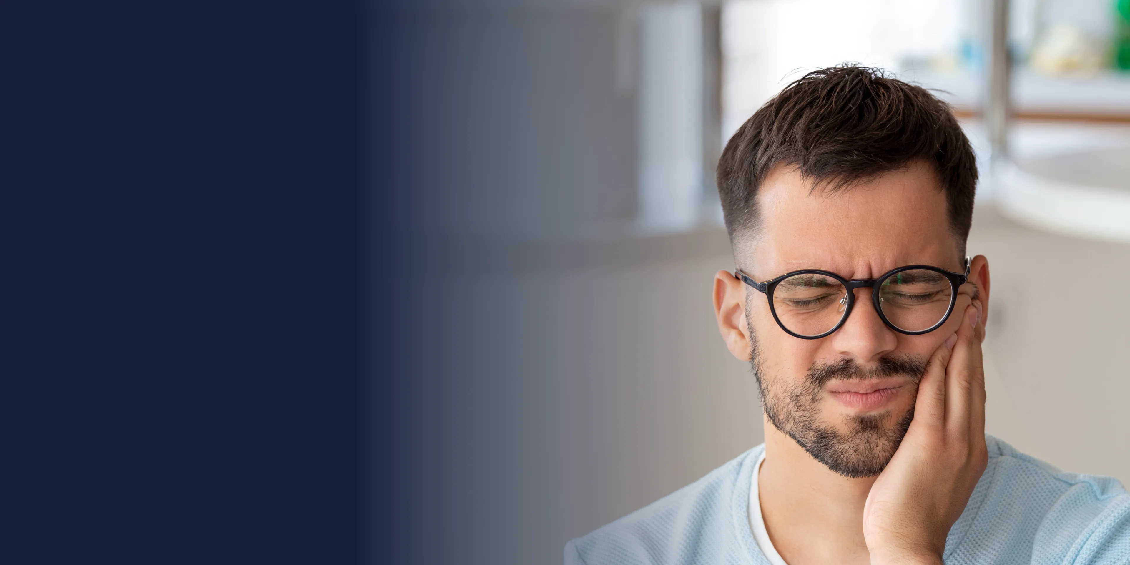 Man sitting at a desk, pressing an ice pack to his cheek.