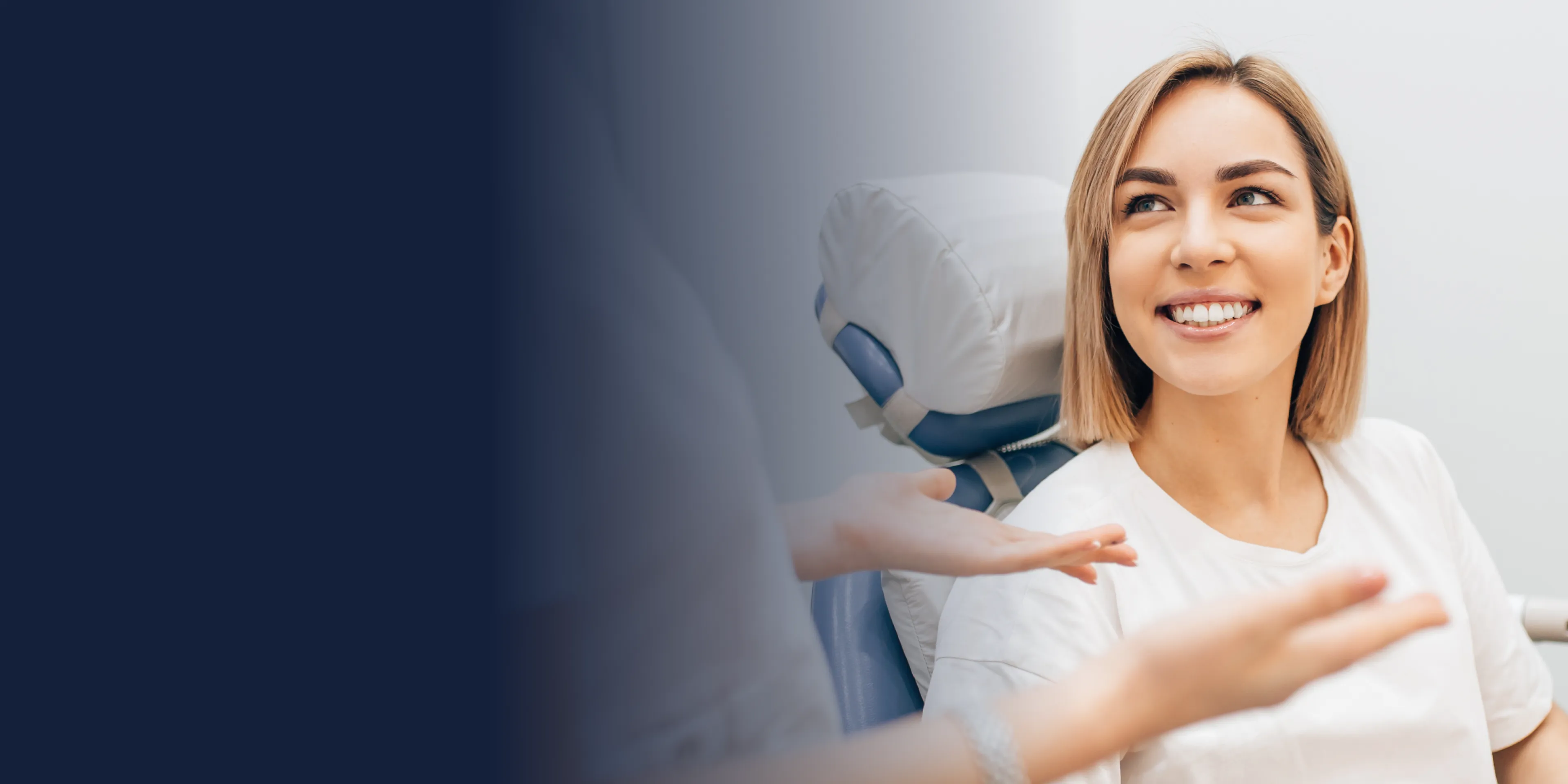 A woman with short hair smiles while sitting in a chair, interacting with someone nearby.