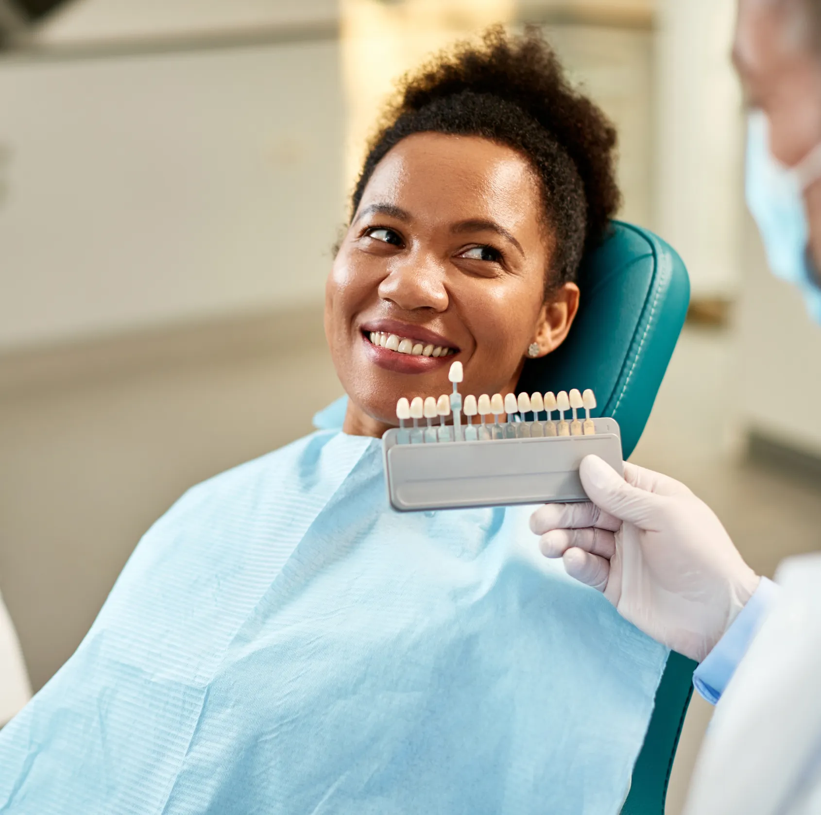 Dentist compares patient's teeth color with a tooth shade guide in a dental clinic.