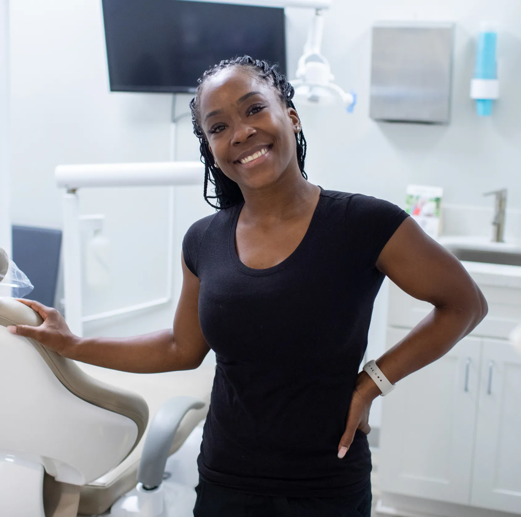 Smiling person standing in a dental clinic next to a dental chair.
