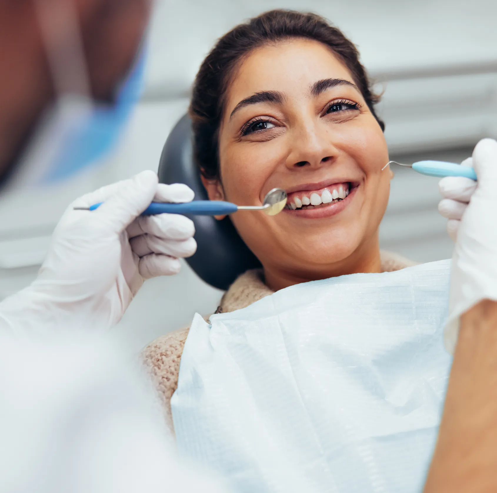 A dentist examines a smiling patient's teeth with dental tools.