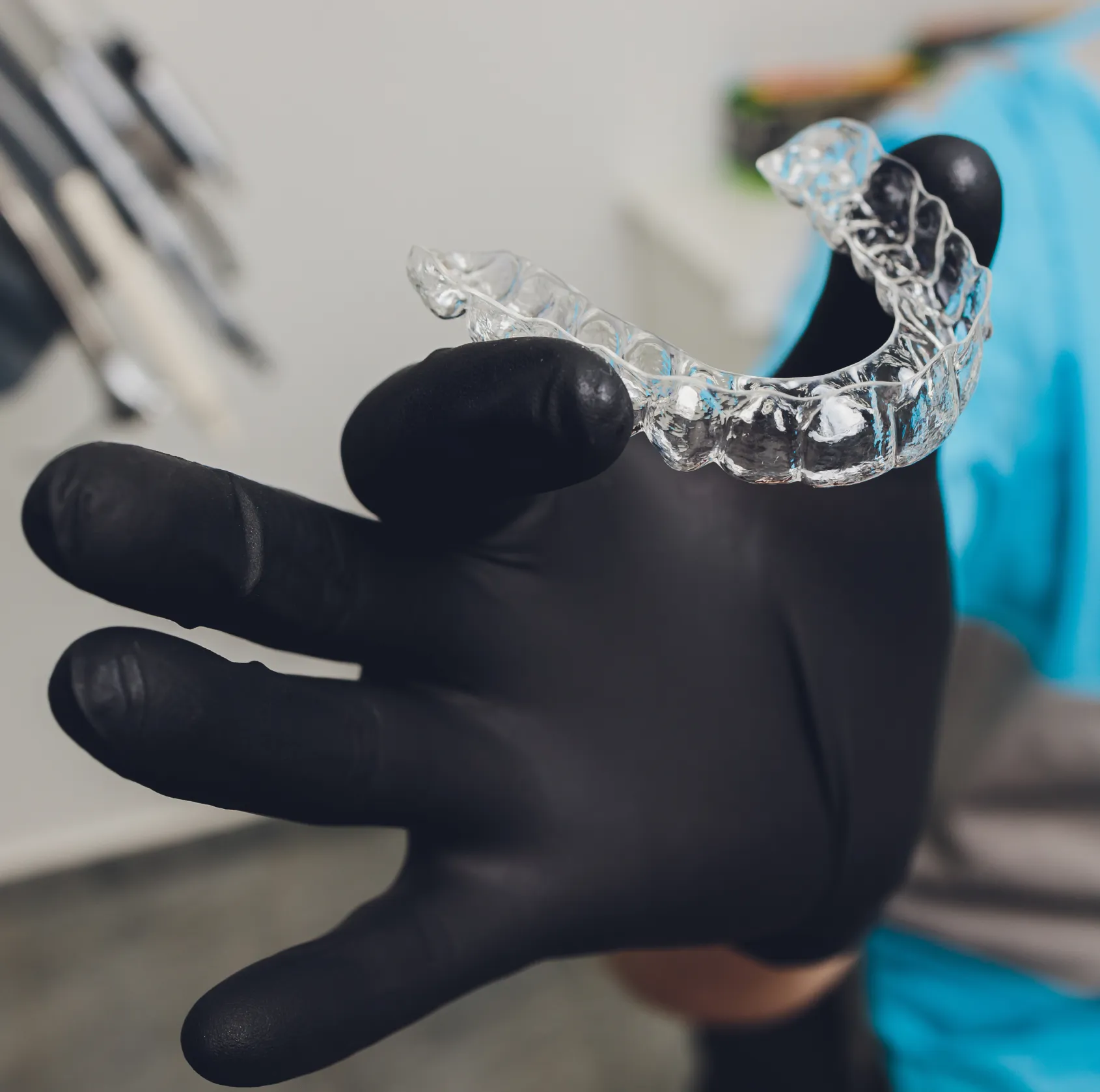 A gloved hand holds a clear dental aligner, emphasizing its transparent material.