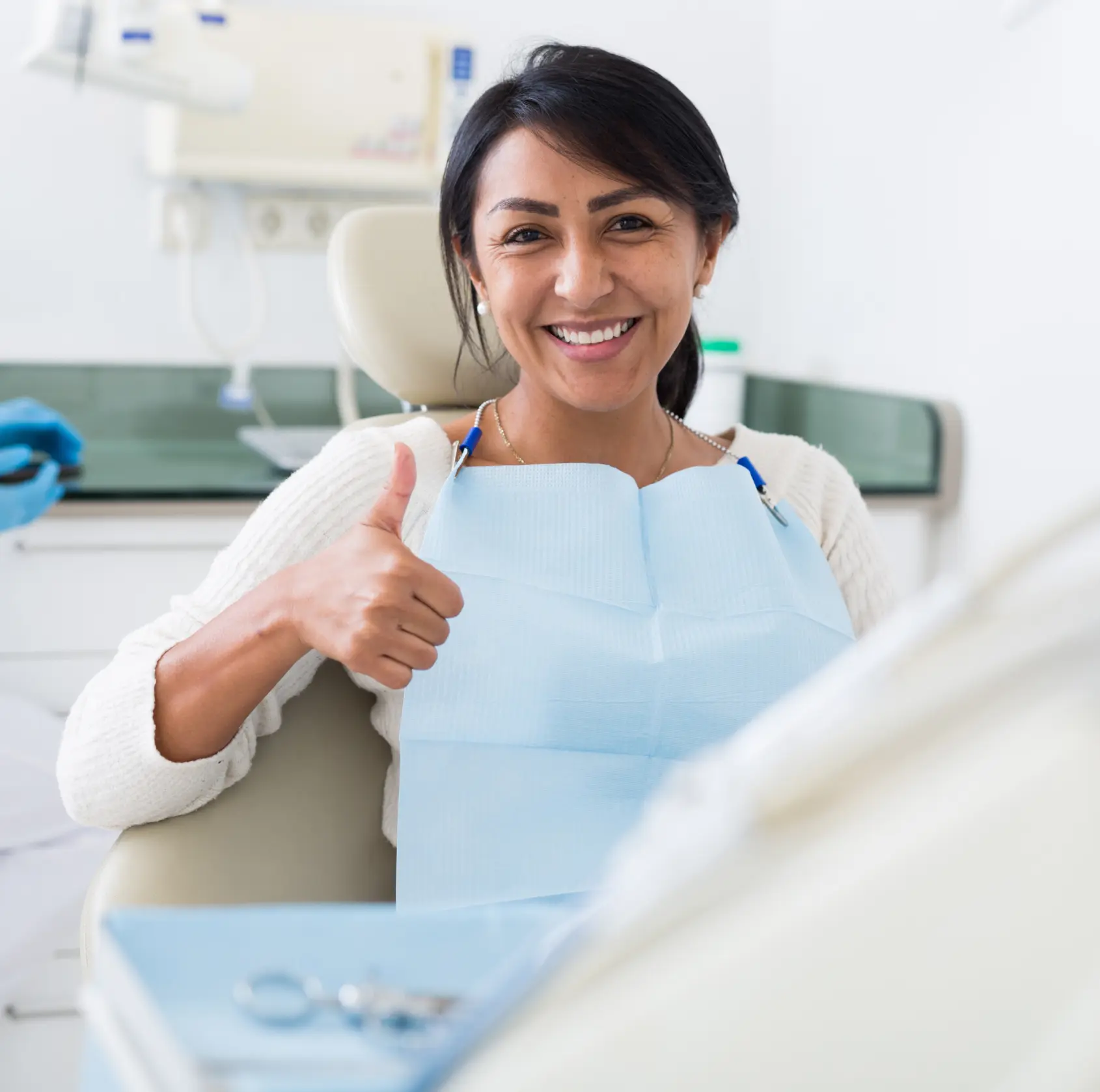 Woman in a dental chair giving a thumbs-up, wearing a dental bib and smiling.
