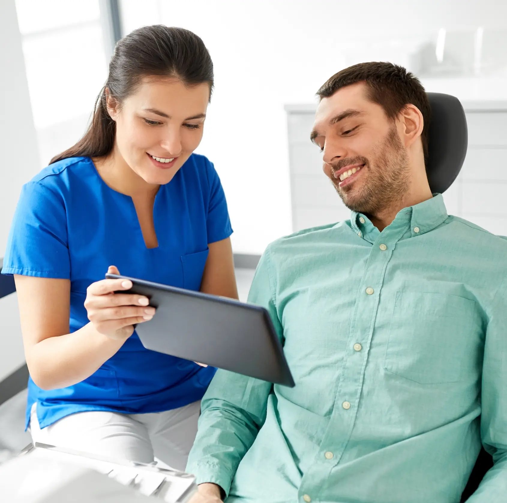 A dental professional shows a tablet to a man sitting in a dentist's chair.