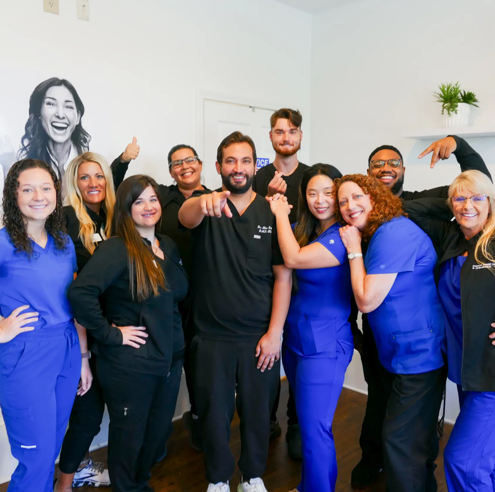 A group of smiling medical staff in scrubs and jackets posing together in an office.