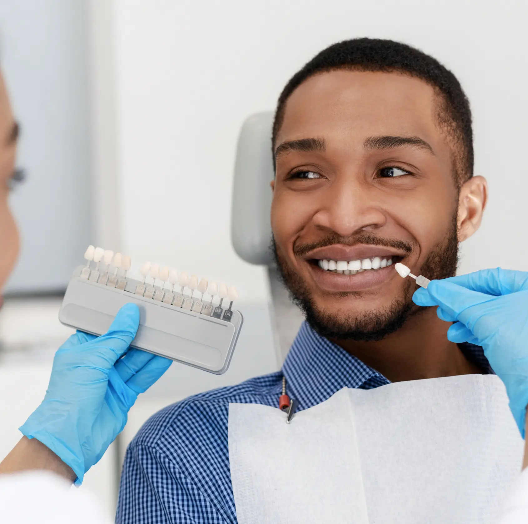Dentist holding a tooth shade guide next to a patient smiling in a dental chair.