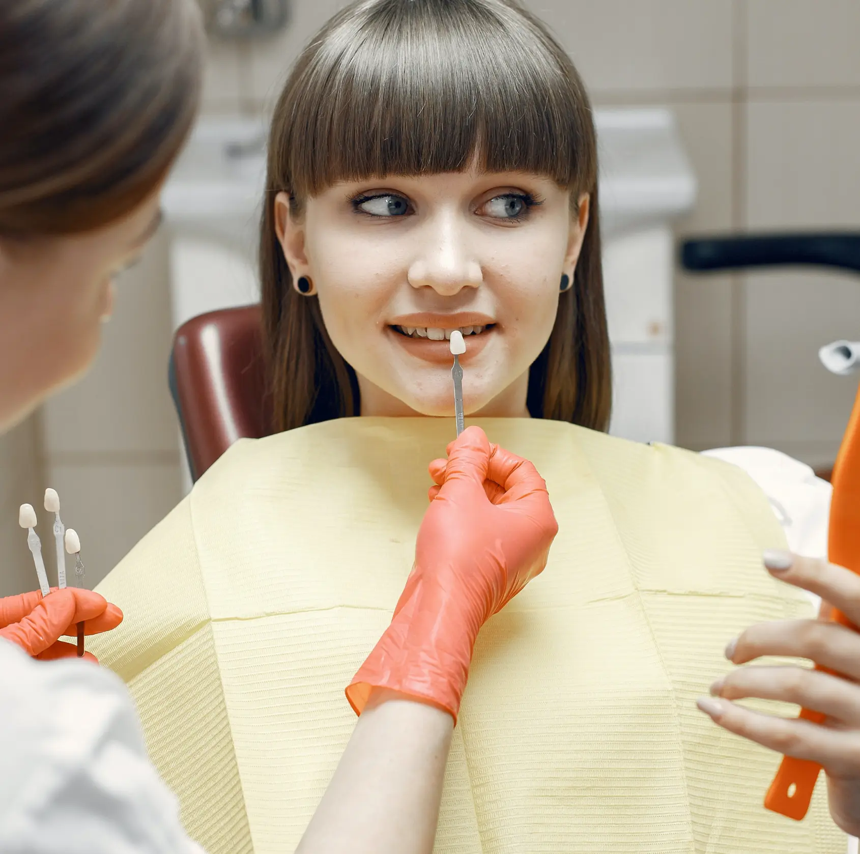 A dentist compares tooth shades to a young woman’s teeth during a dental appointment.