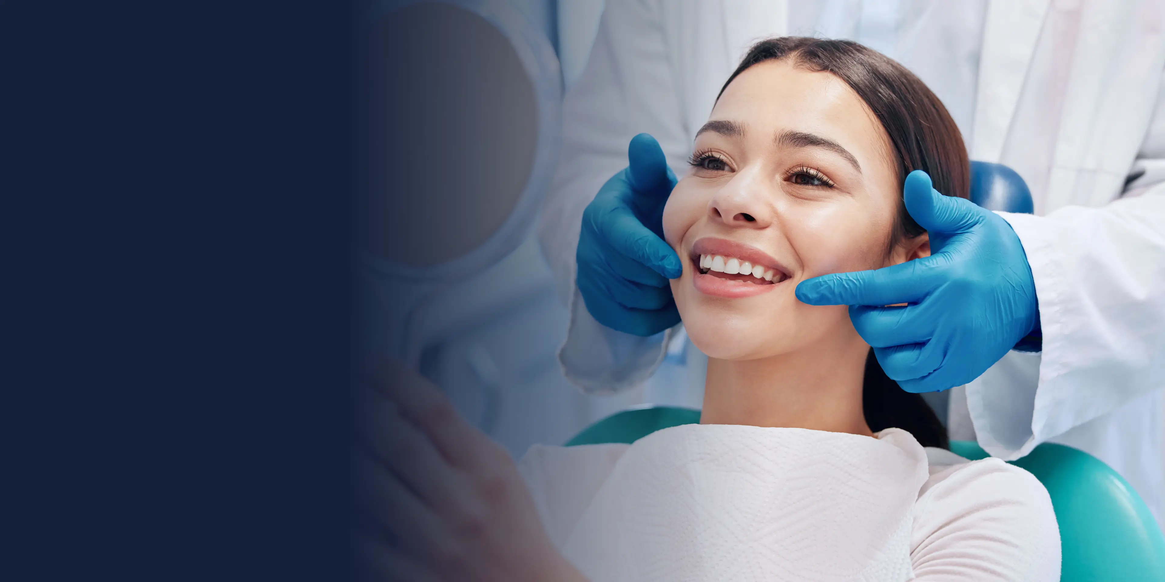 Dentist in blue gloves examines a smiling woman's teeth in a dental chair.