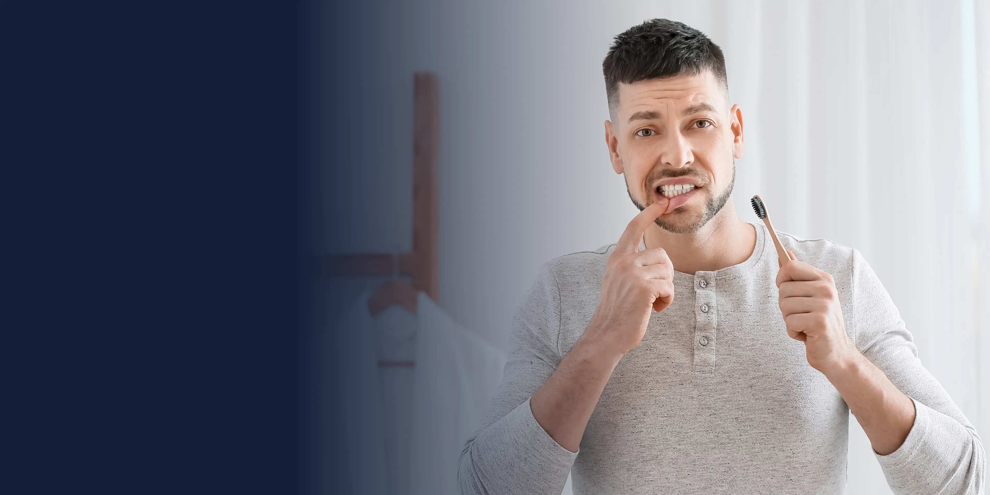 Man holding toothbrush, pointing at his teeth, in a room with a blue gradient background.