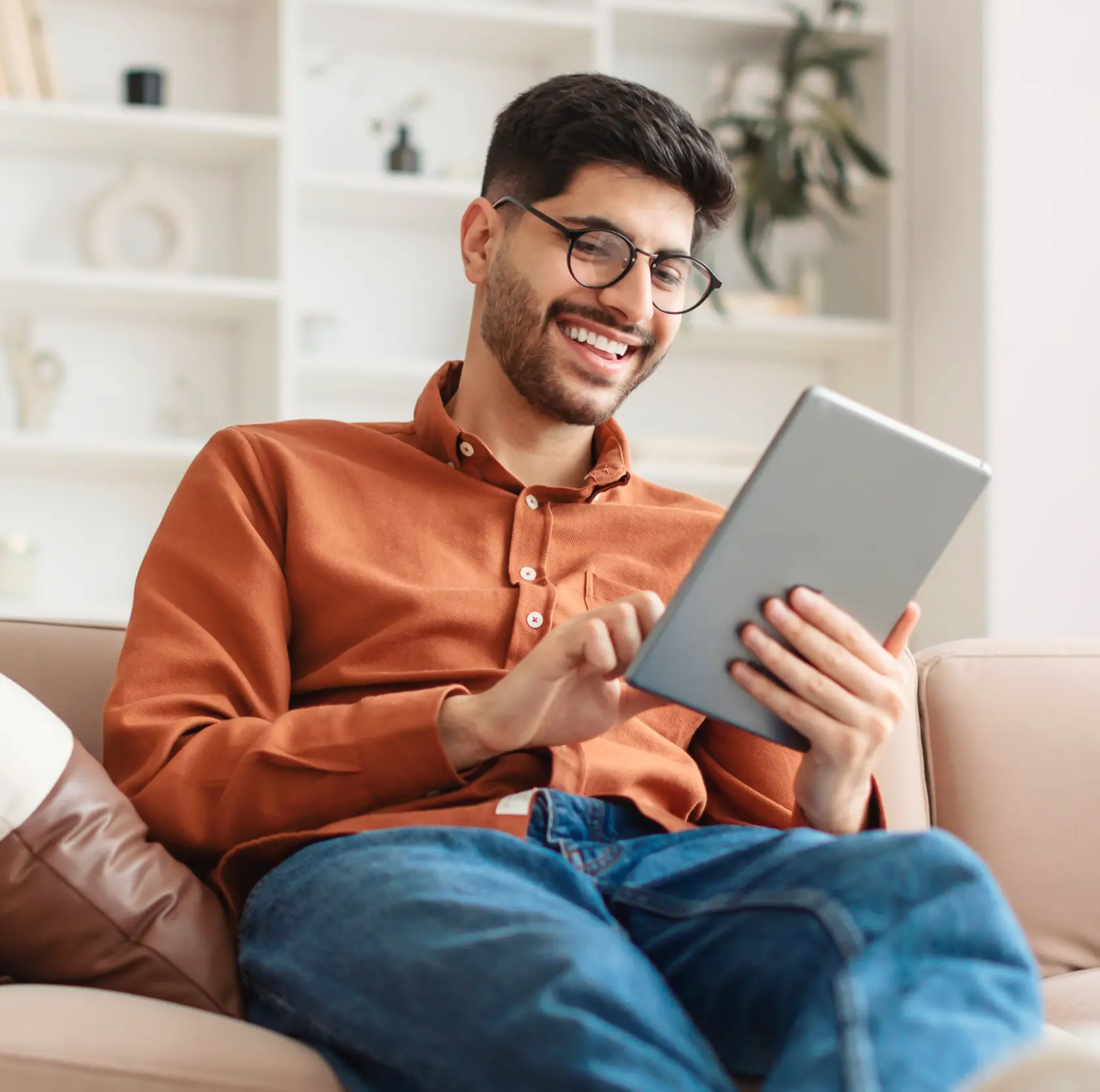 Man sitting on a couch, smiling while using a tablet.
