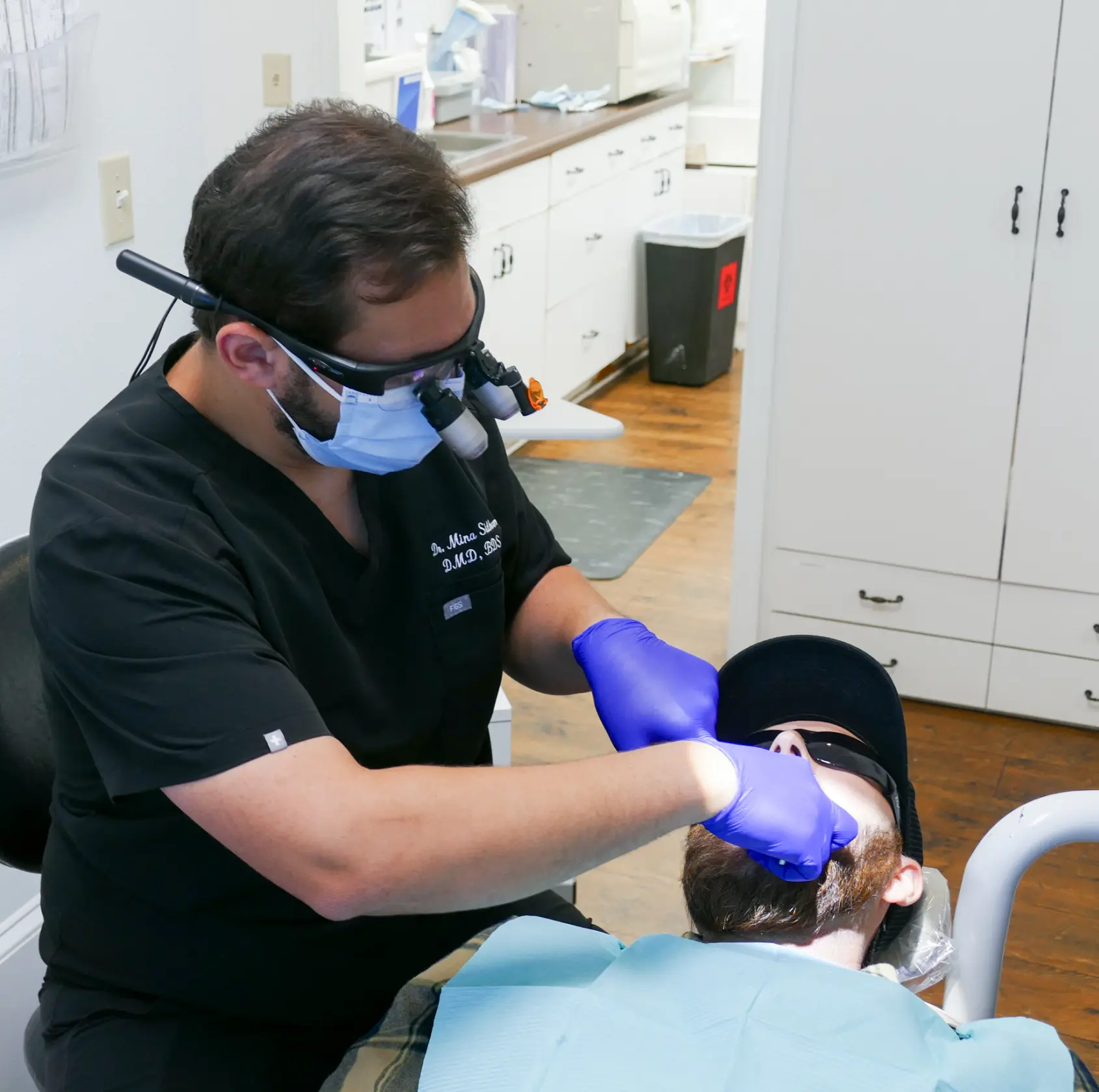A dentist wearing gloves and a mask examines a patient's mouth in a dental clinic.
