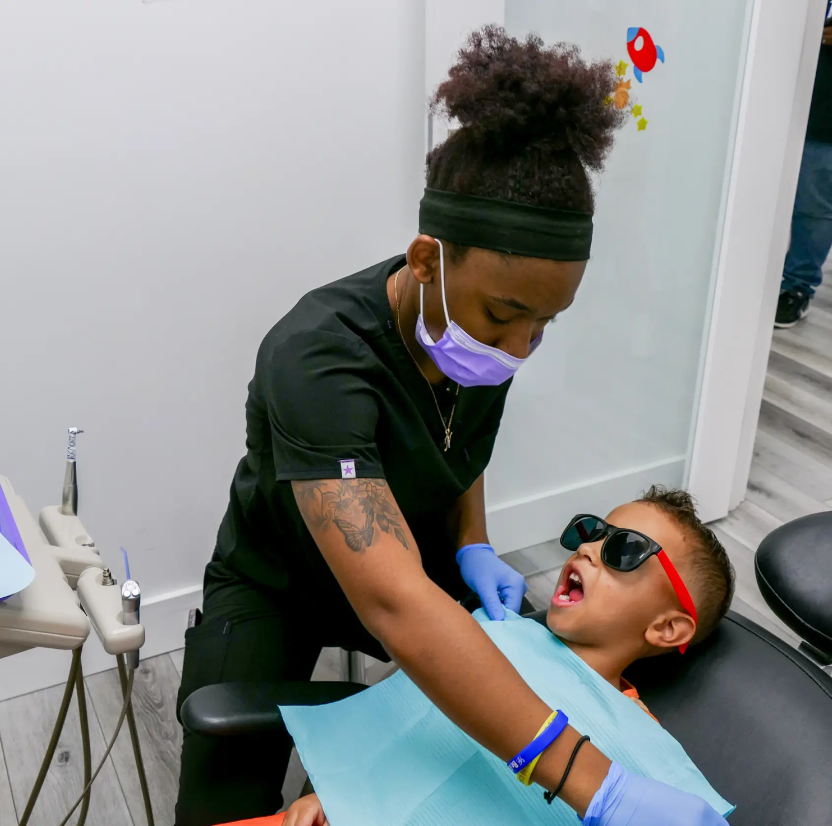 Dental hygienist checking a child's teeth in a clinic. The child is wearing sunglasses.