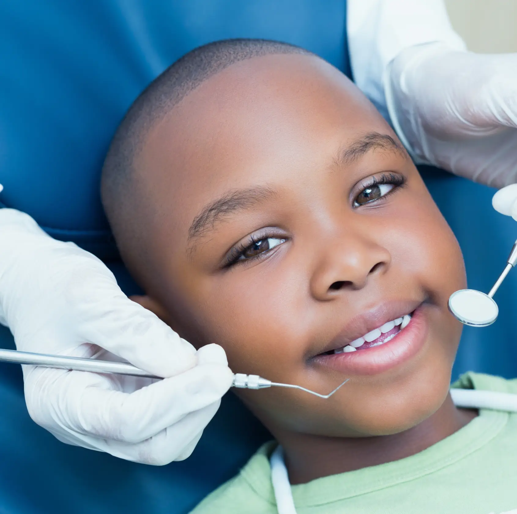 A child receives a dental check-up from a dentist holding tools near their mouth.