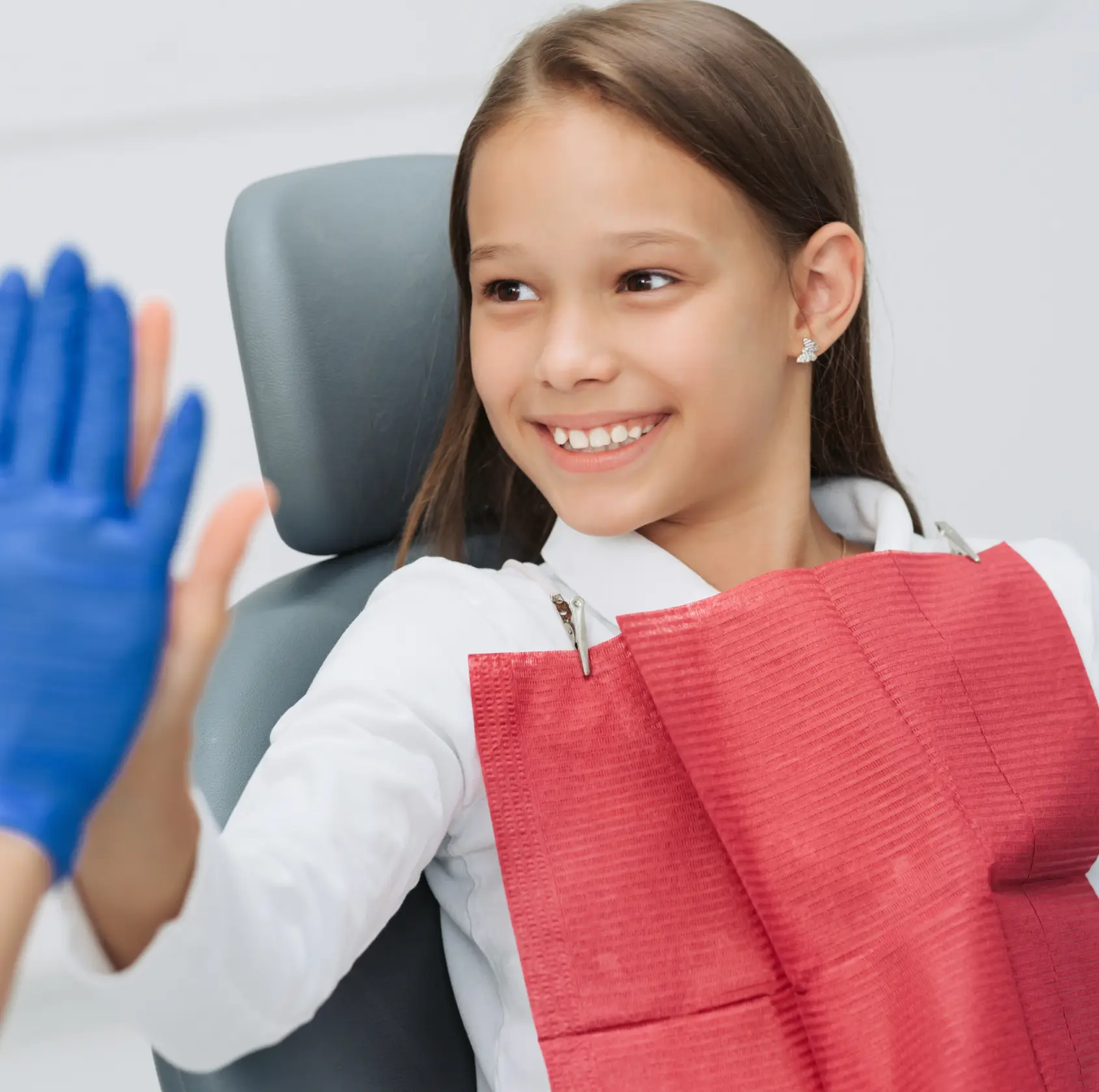 A young girl in a dental chair high-fives a person wearing blue gloves.