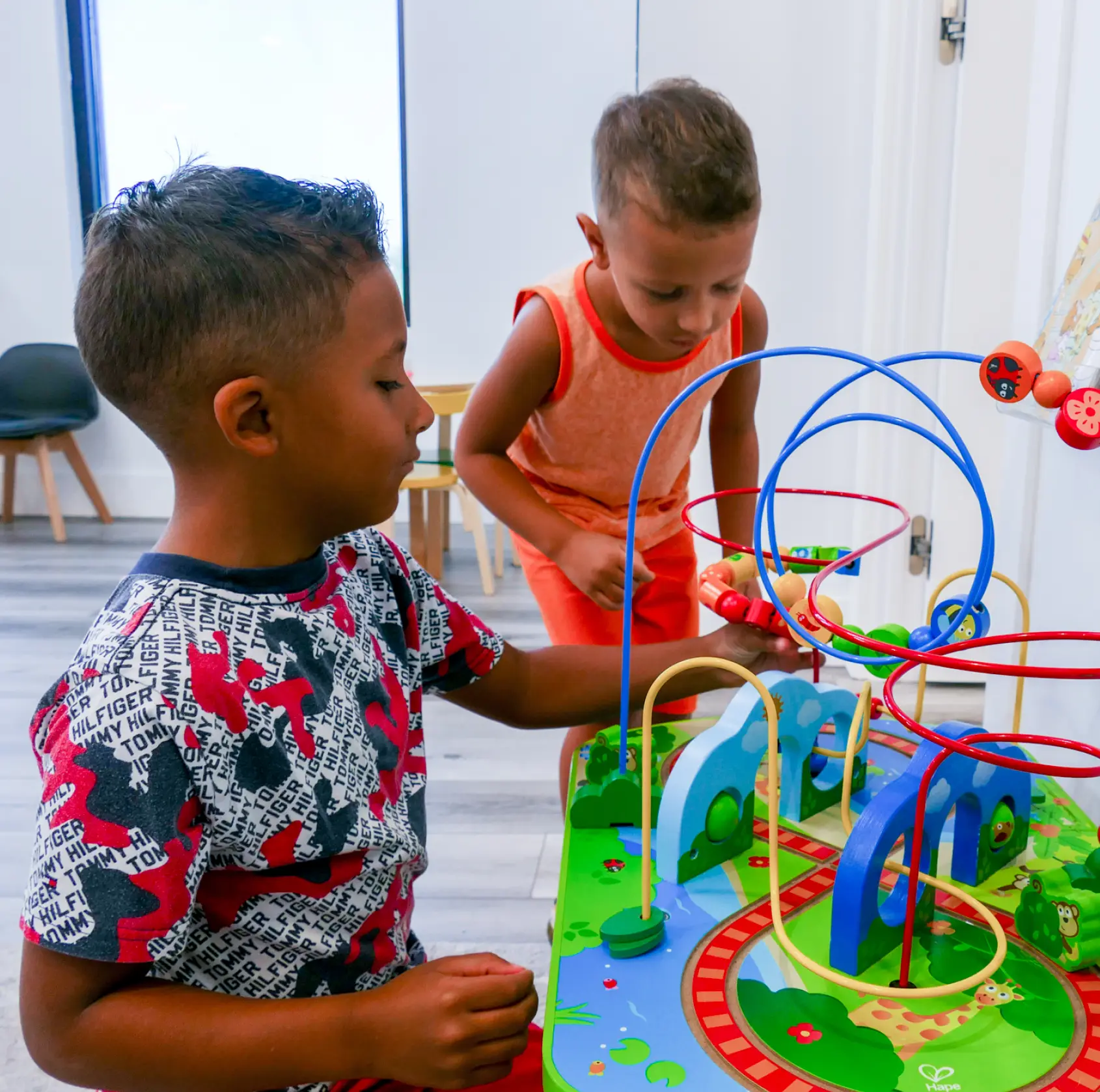 Two children play with an educational toy featuring colorful wires and beads indoors.