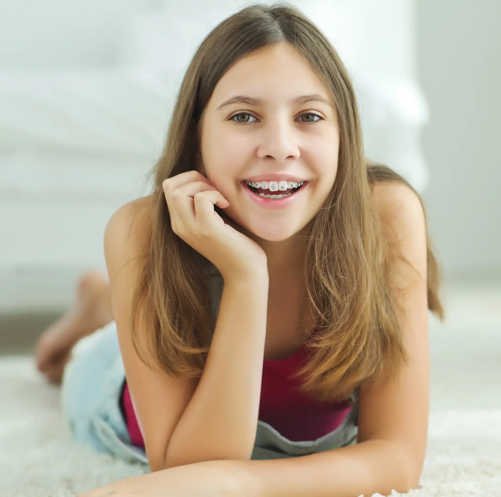 Teenage girl with braces lying on a rug, smiling and resting her chin on her hand.