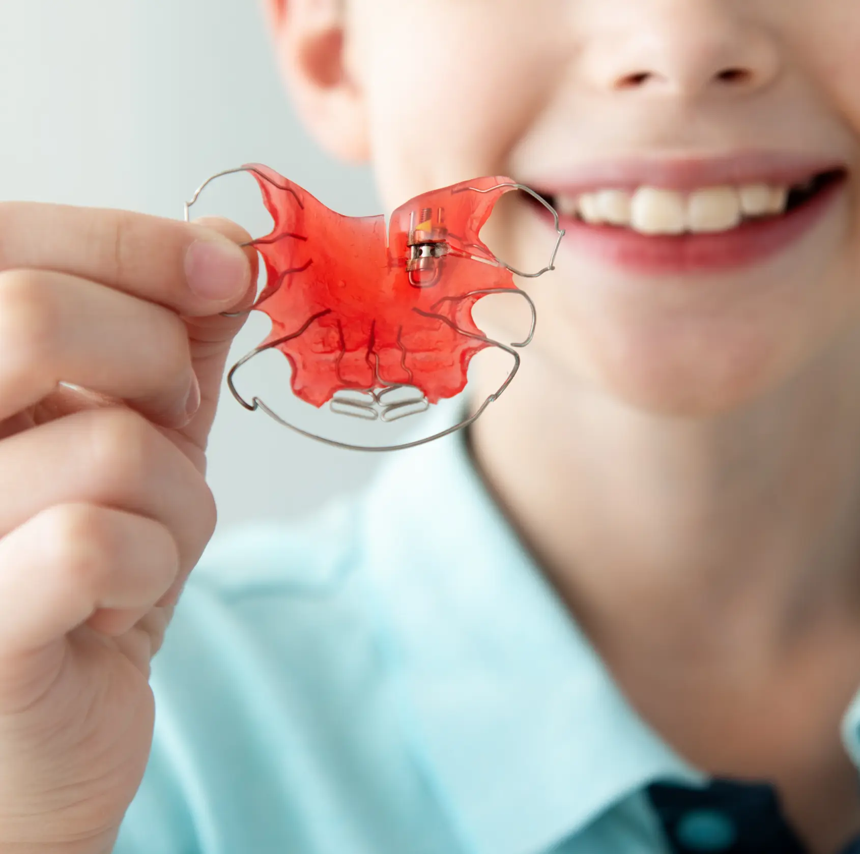 Smiling child holding a pink dental retainer close to the camera.