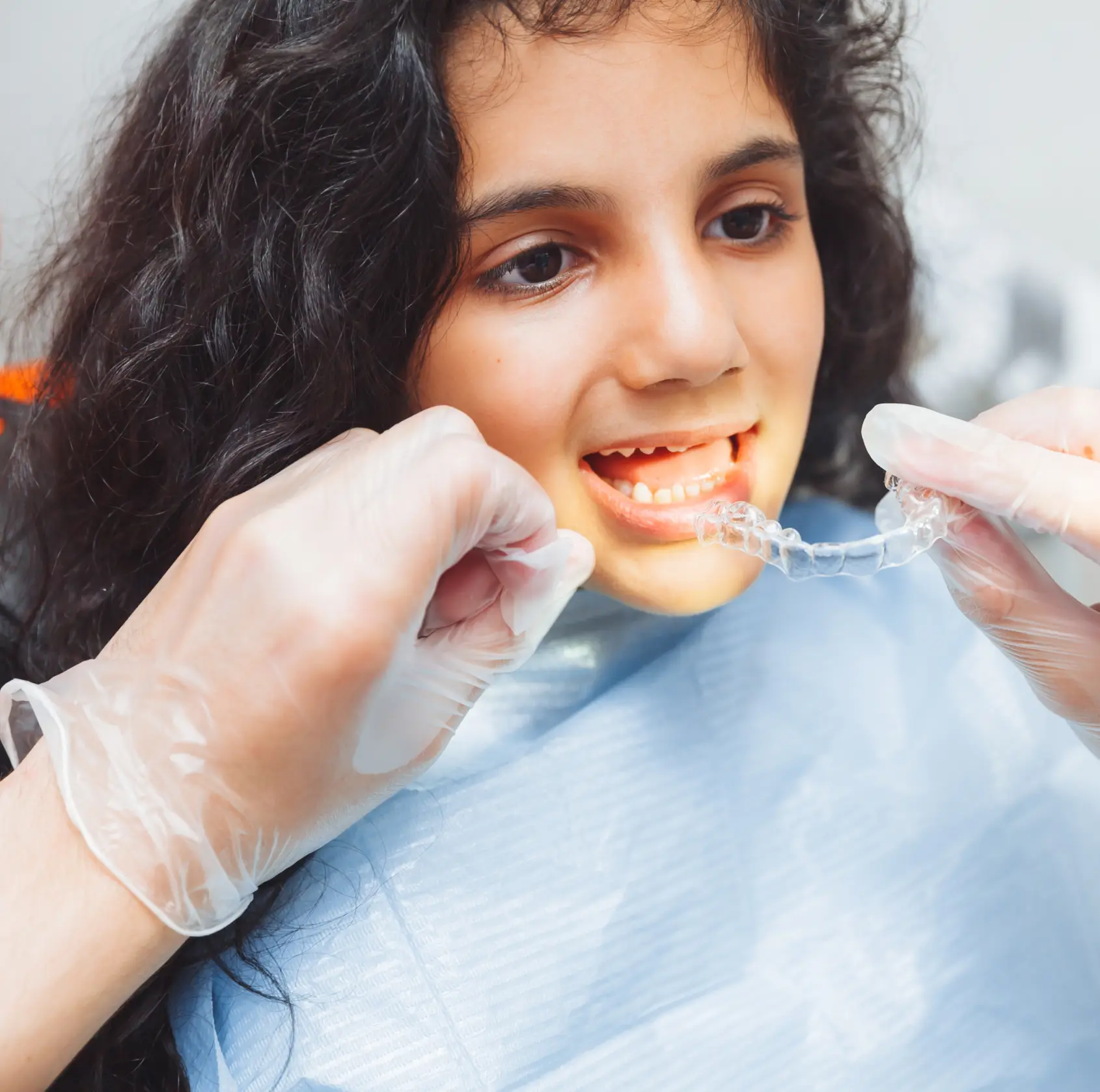 A dentist fits a transparent dental retainer onto a young girl's teeth.