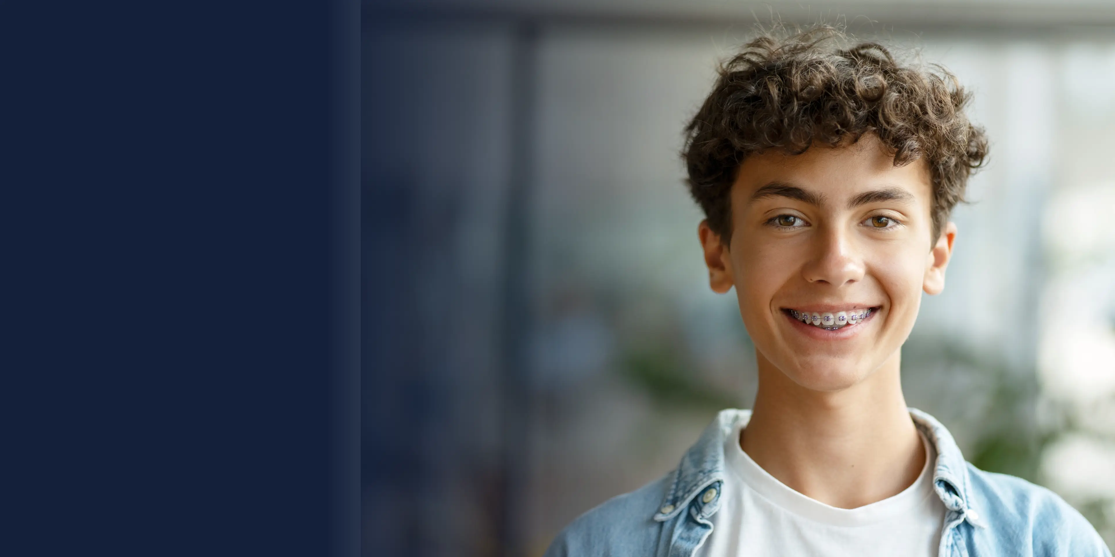 Smiling young person with curly hair and braces, wearing a denim jacket and white shirt.