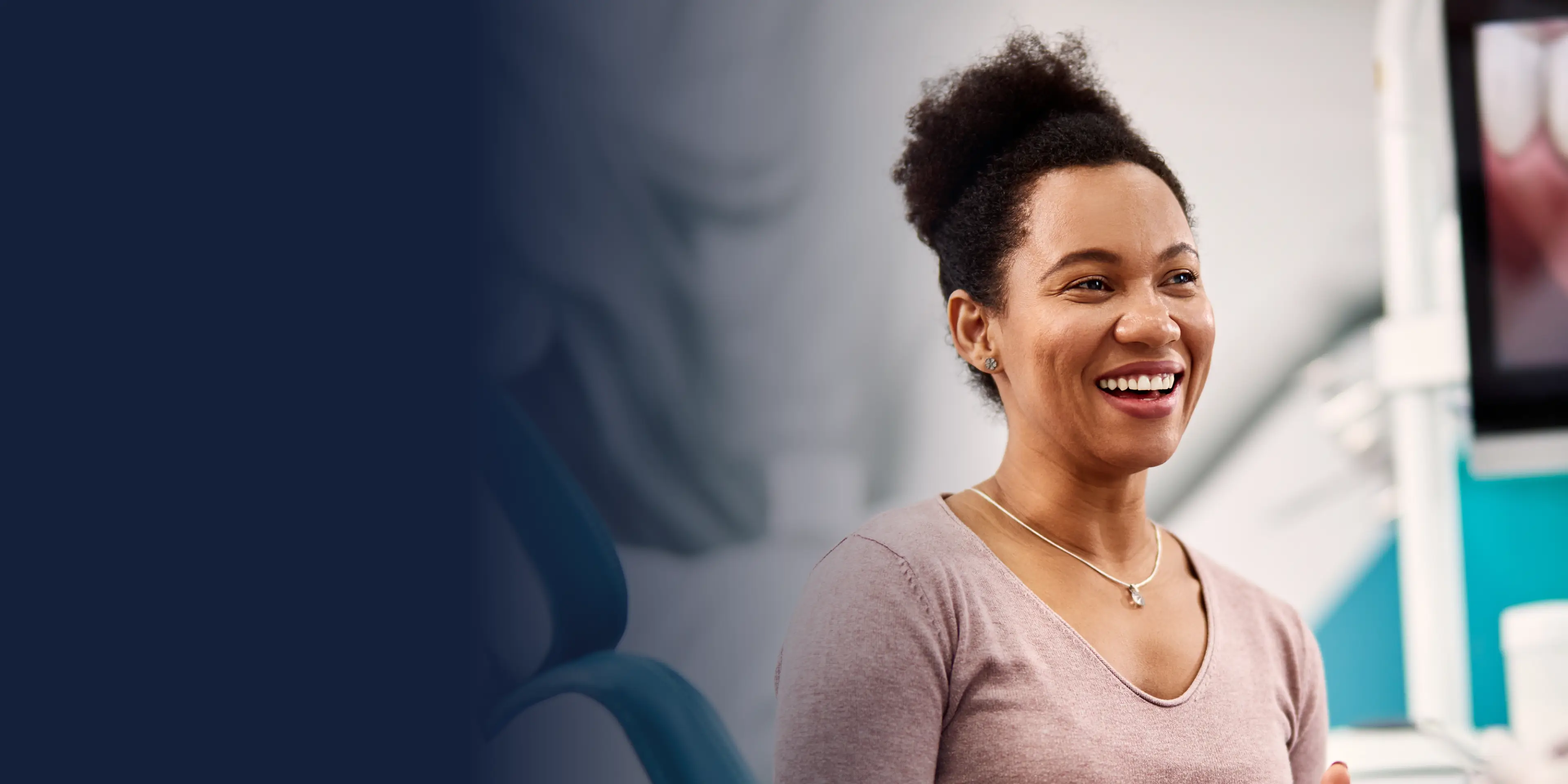 Smiling woman with curly hair wearing a necklace in an office or clinic setting.