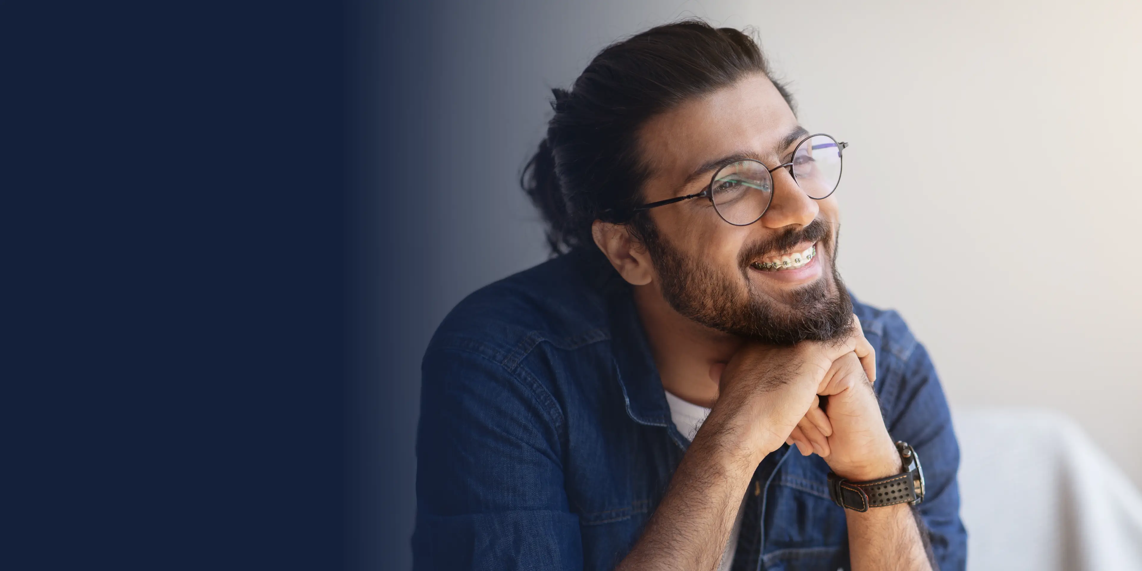 Smiling man with glasses and a beard, wearing a denim shirt, looking to the side.