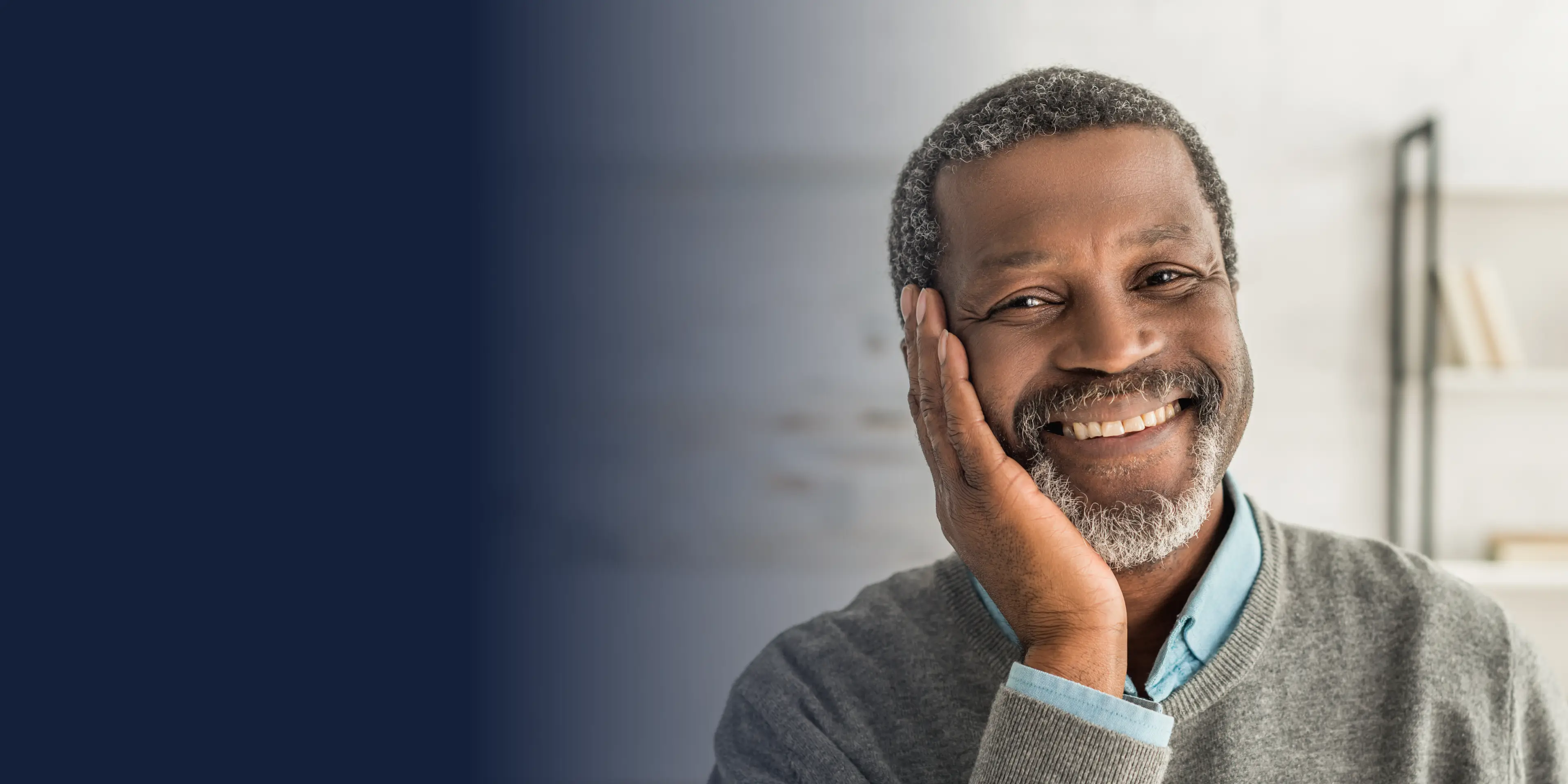 A man with a beard smiling, resting his head on his hand in a relaxed pose.