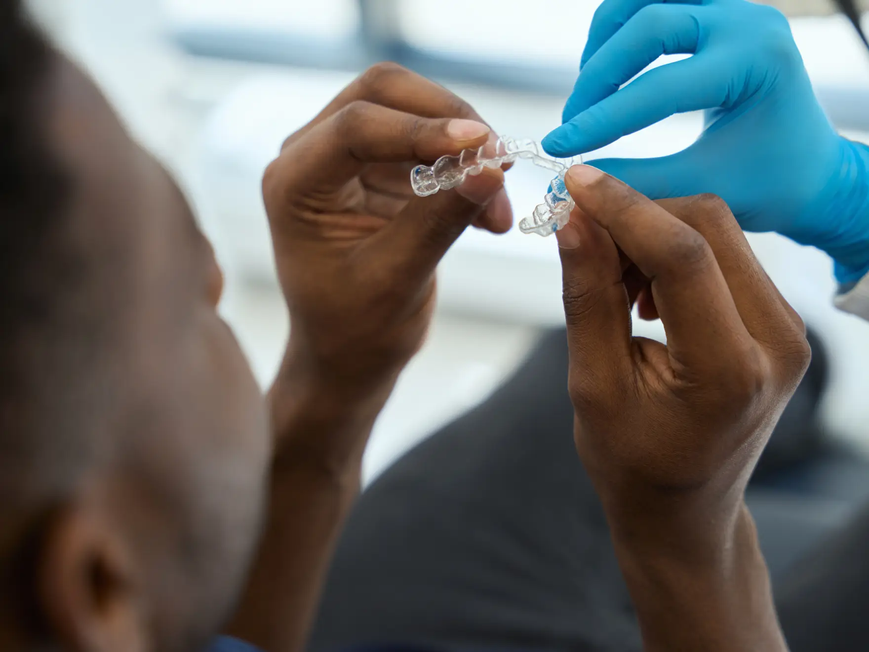 A person examines a dental aligner held by a gloved hand.