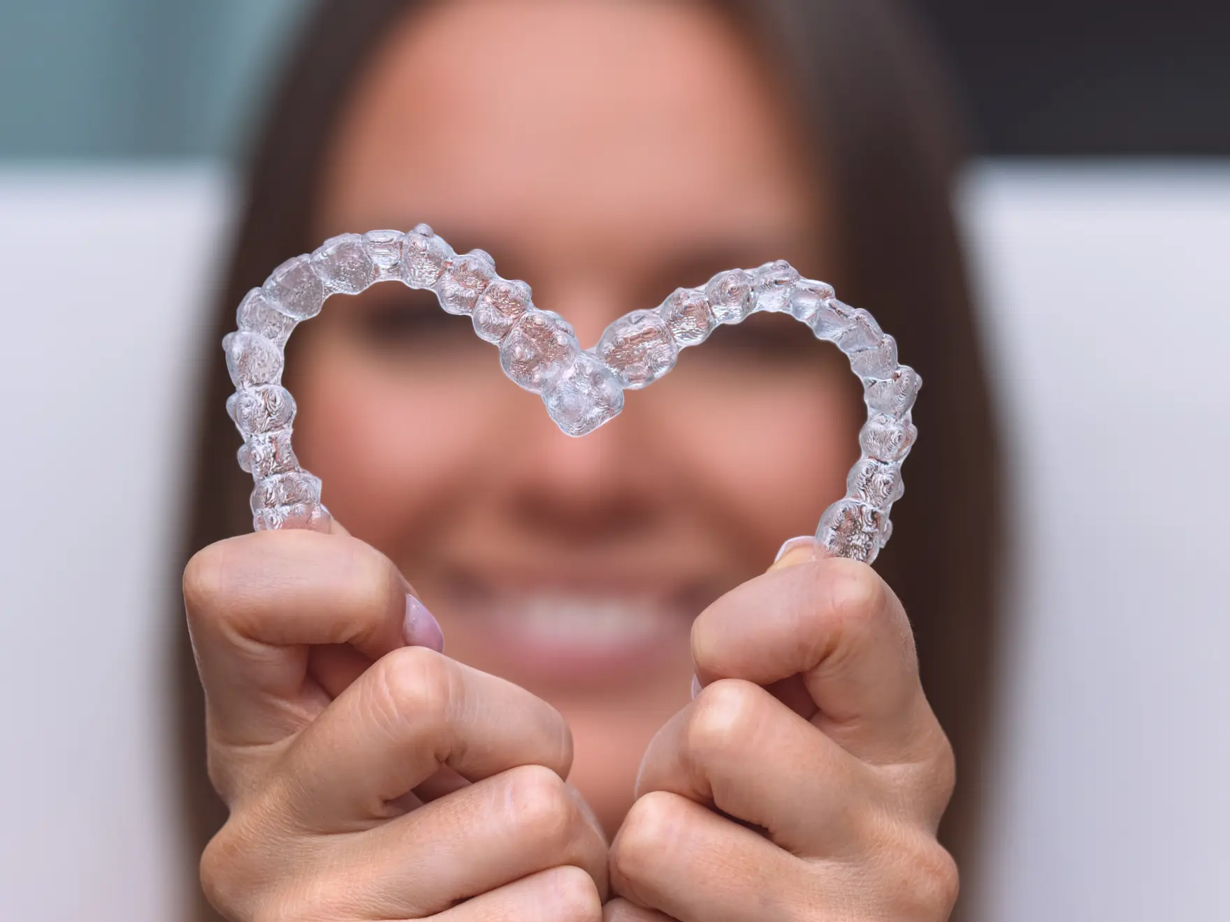 A person holds two transparent dental aligners together to form a heart shape.