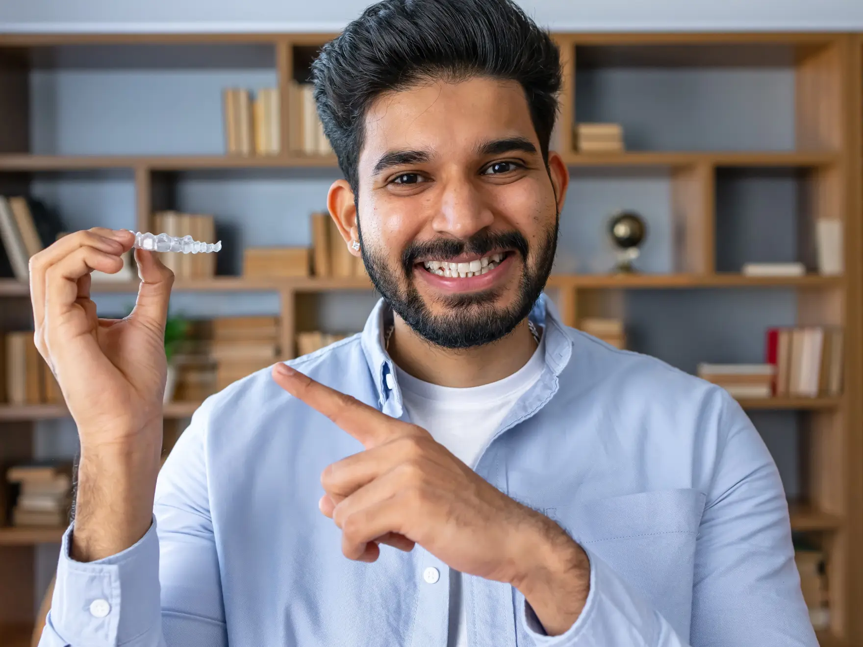 Man smiling and holding a dental aligner, pointing at it with the other hand.