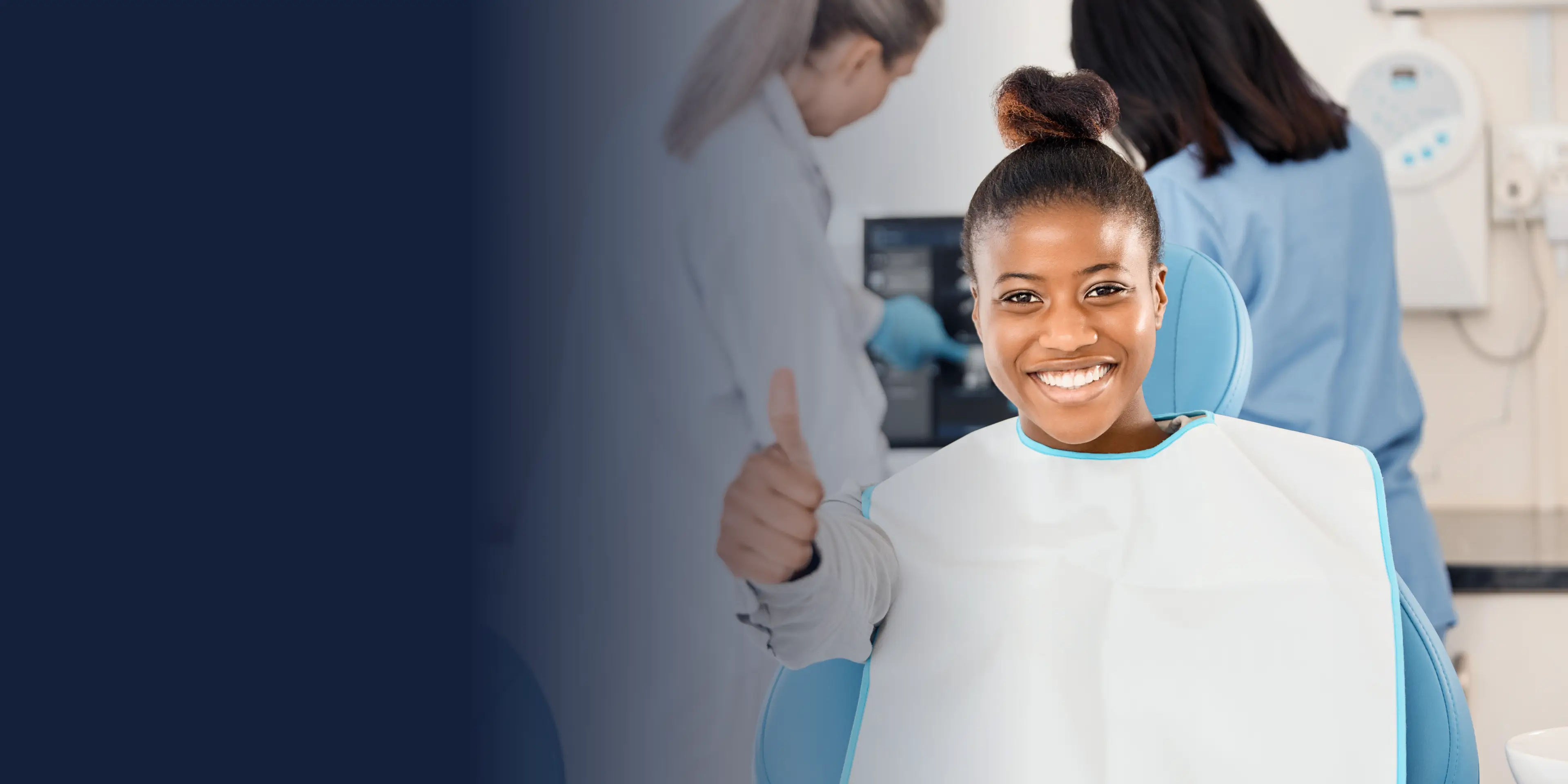 A person sitting in a dental chair giving a thumbs-up, with dental staff in the background.