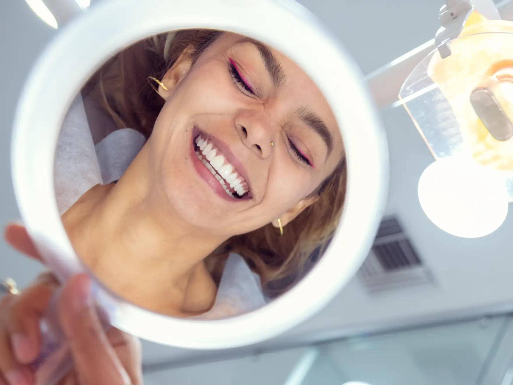 Woman smiling and looking into a circular mirror, showing her reflection.