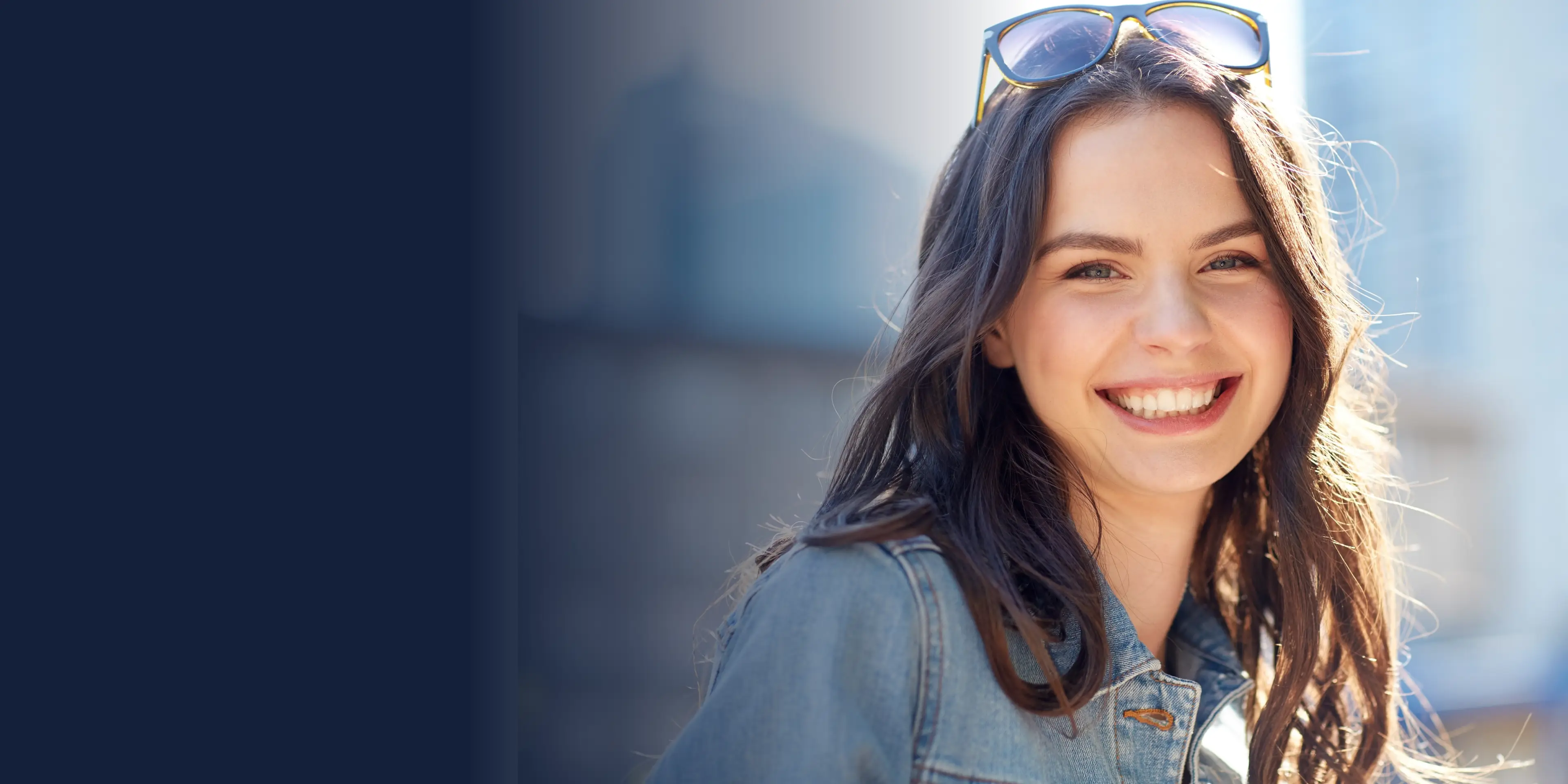 Smiling woman with long hair wearing sunglasses and a denim jacket.
