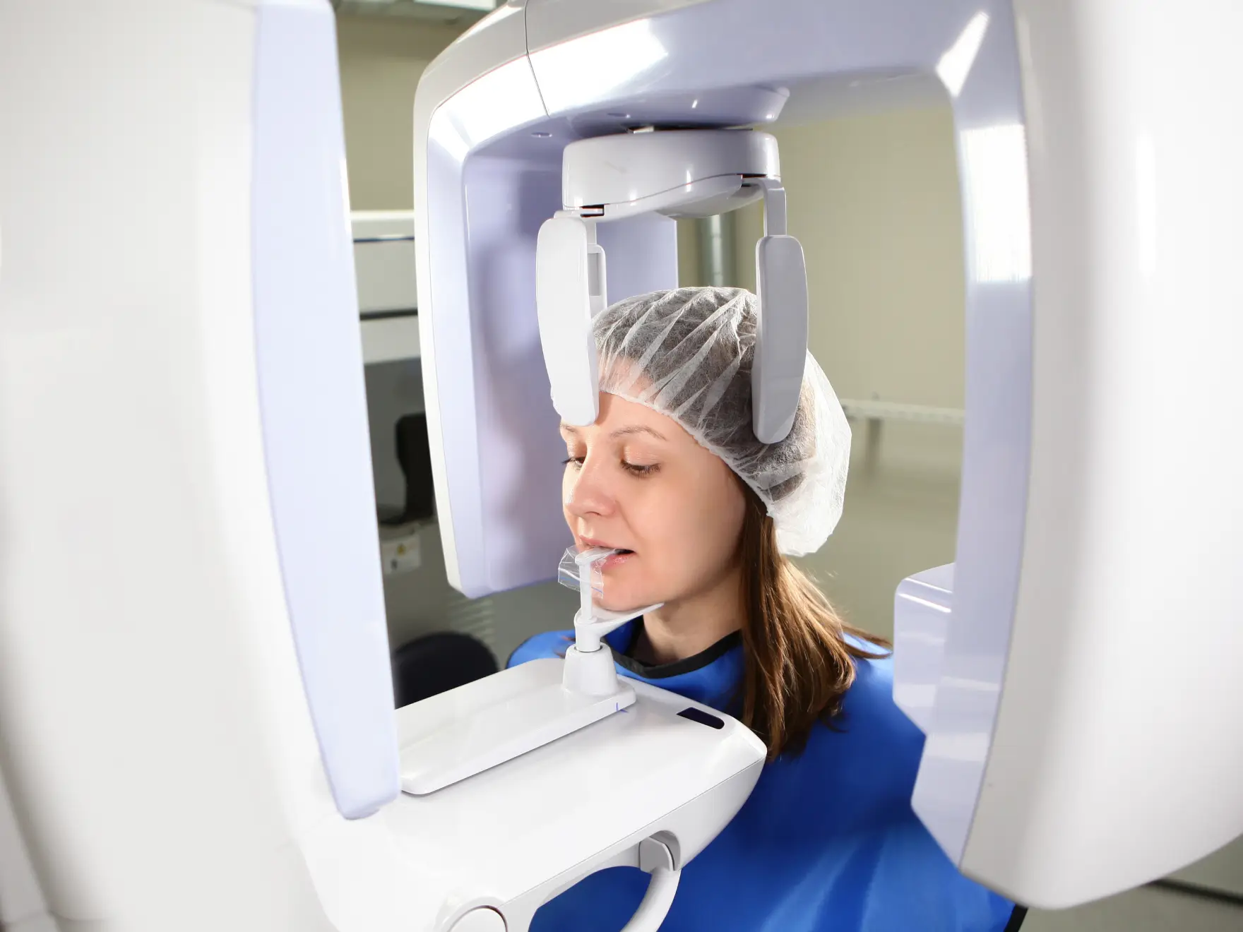 A woman wearing a hair cover undergoes a dental X-ray in a medical facility.