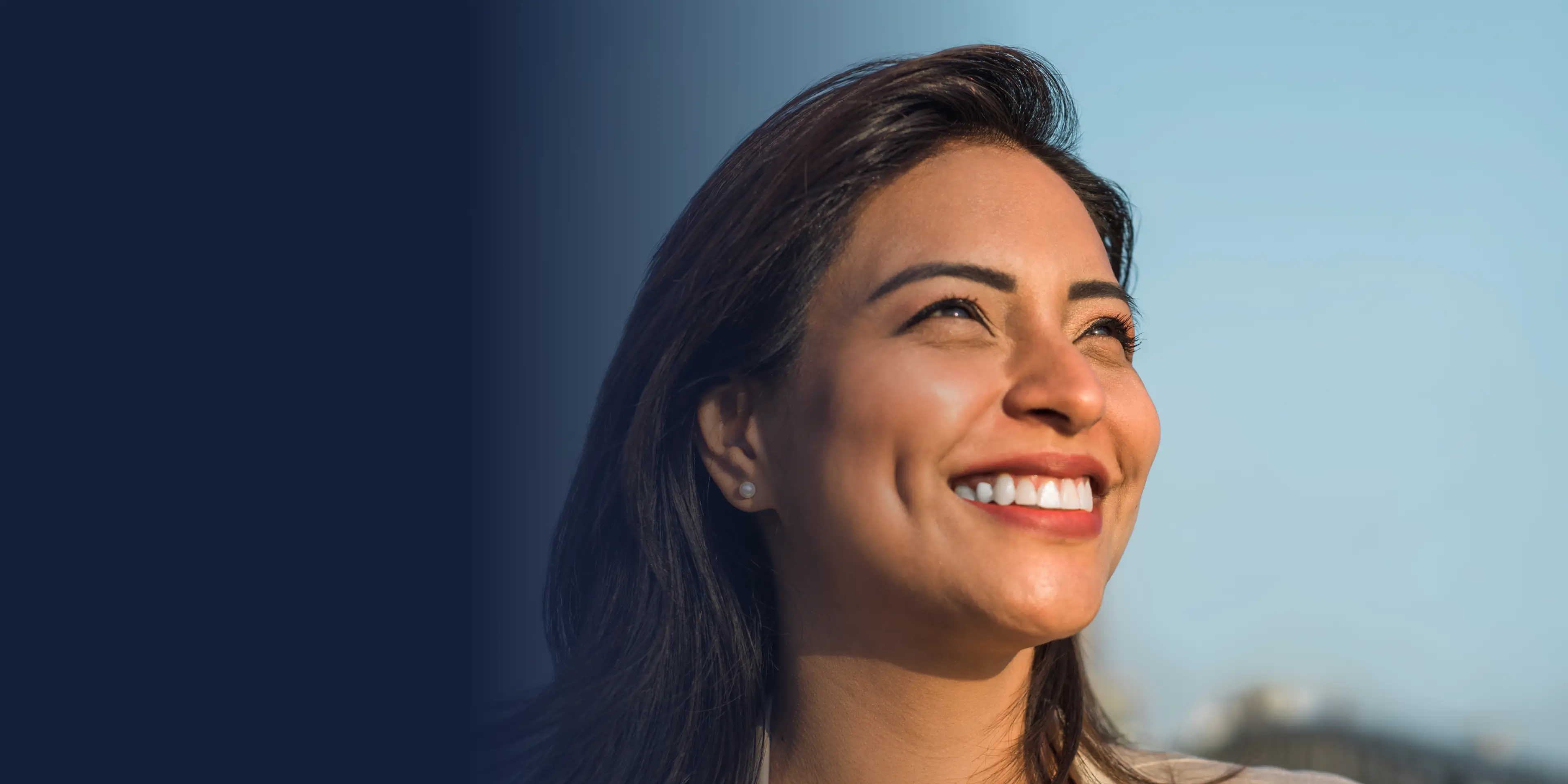 Smiling woman looking up against a blue sky.