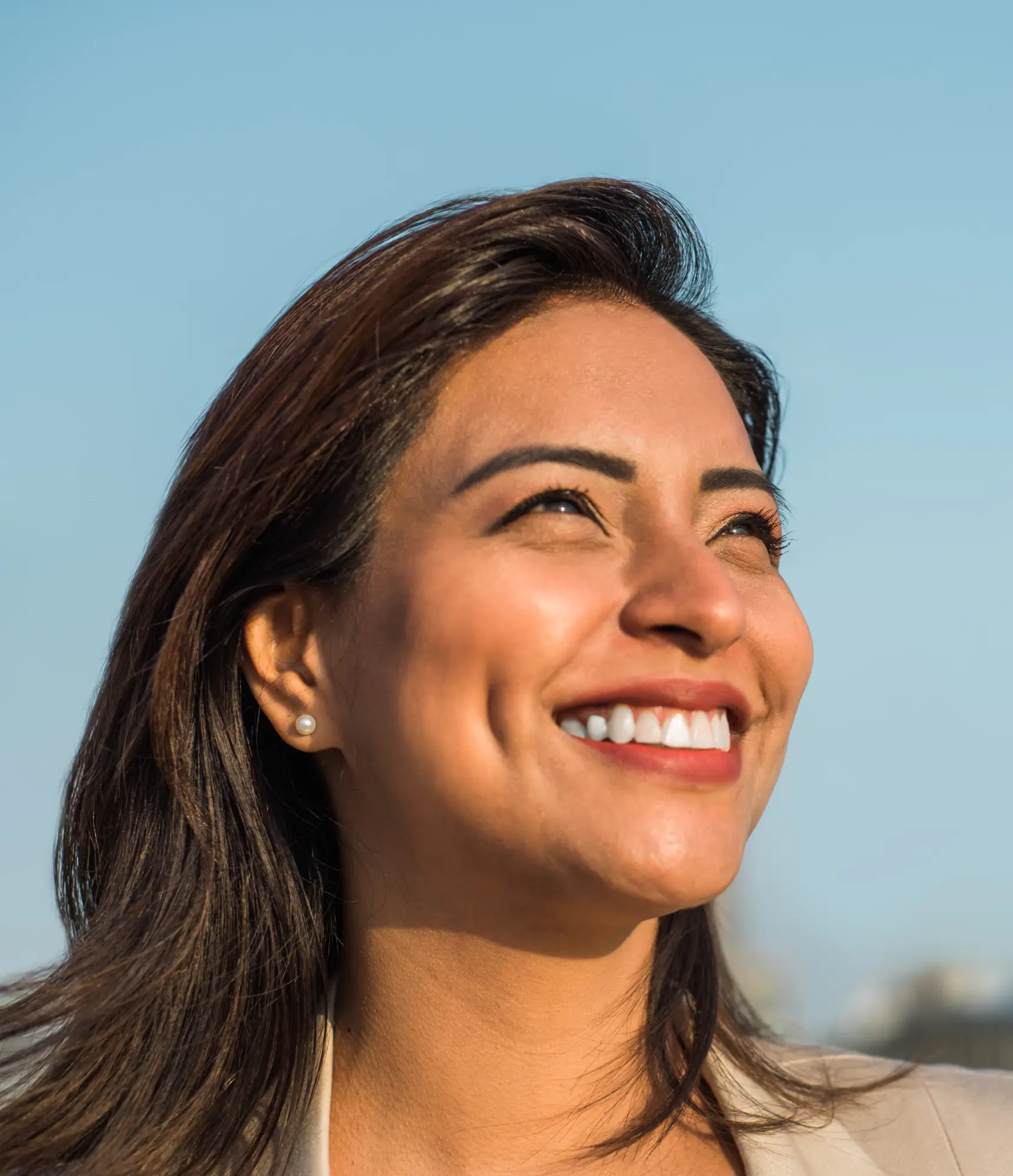 A person smiling while looking up against a clear blue sky.