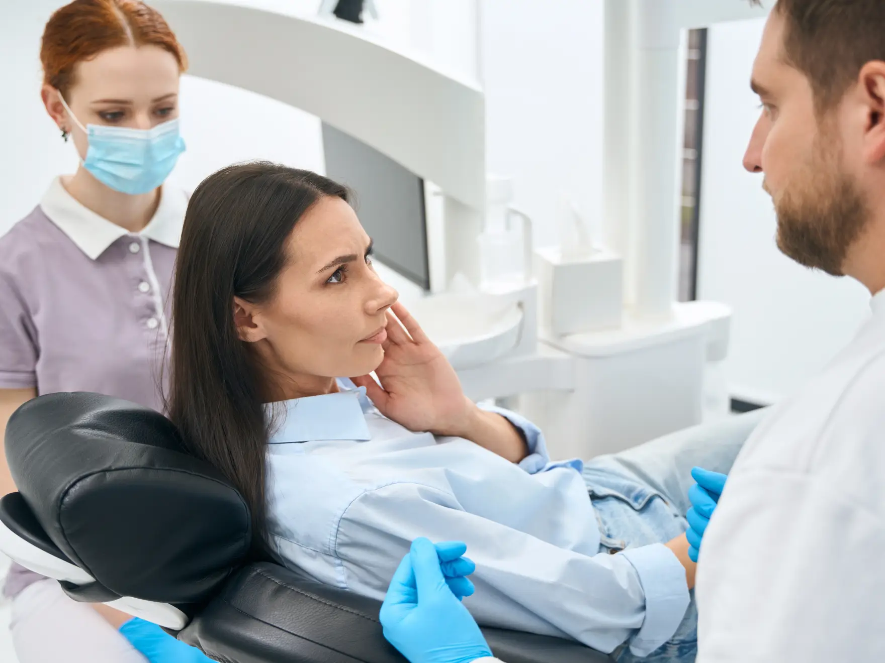 A woman sits in a dental chair with a dentist and assistant examining her.