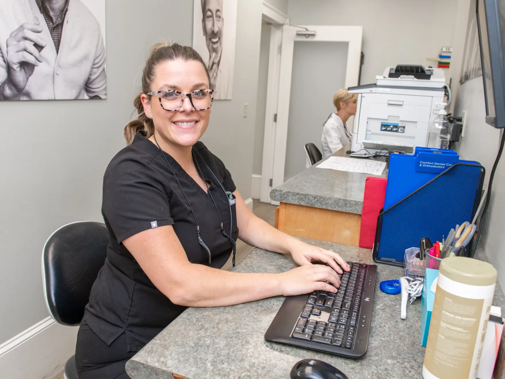 A woman in a black uniform smiles while typing on a keyboard at a reception desk.