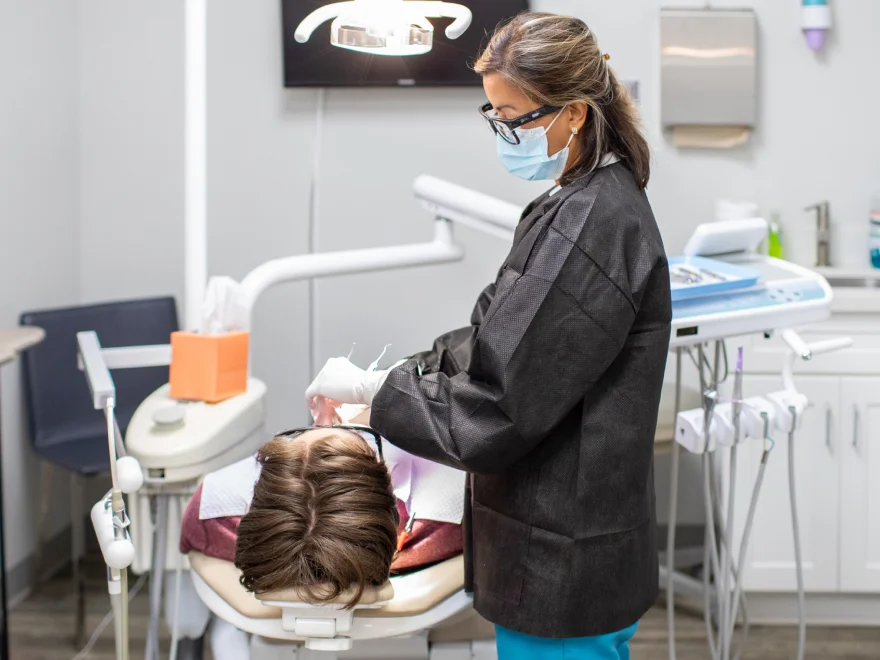 A dentist wearing a mask examines a patient's teeth in a dental office.