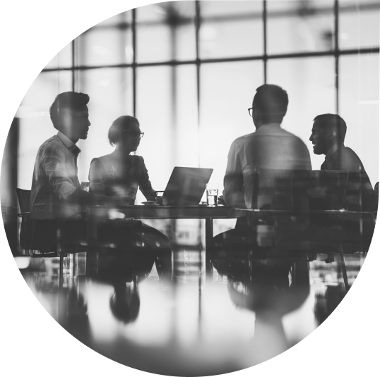 Silhouetted professionals in a meeting around a table with laptops in an office with large windows.