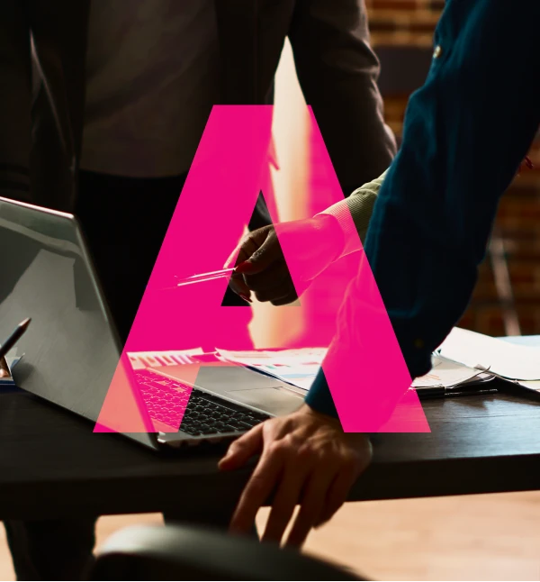 Two people collaborating over a laptop and documents on a desk in a dimly lit room.