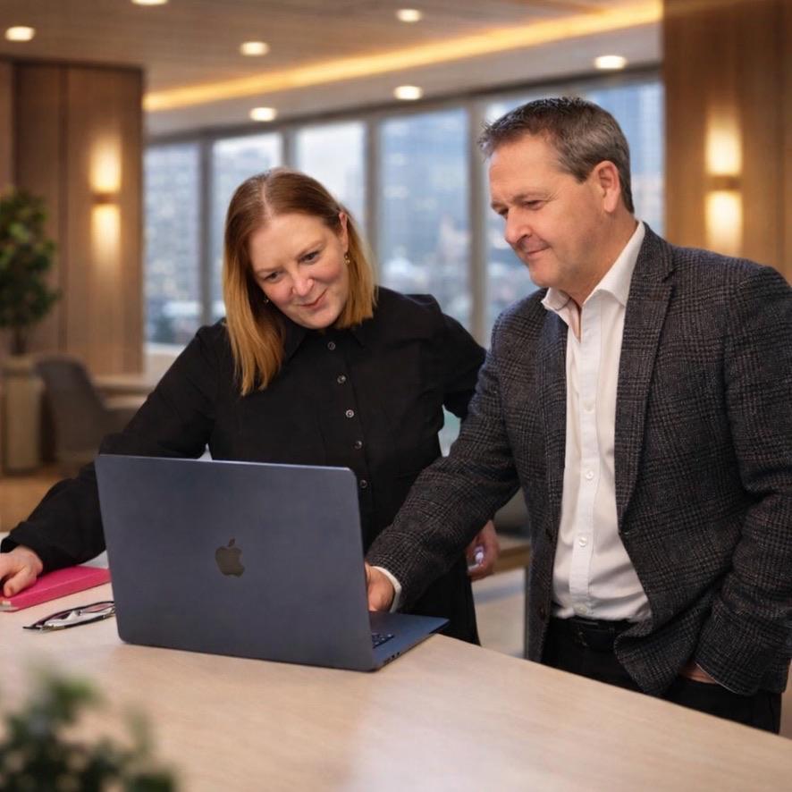 Three colleagues sitting at a conference table, smiling and discussing work with a tablet and documents.