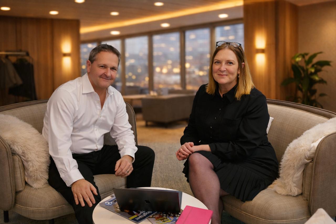 Diverse group of business professionals socializing at a networking event, some holding drinks and using digital devices.