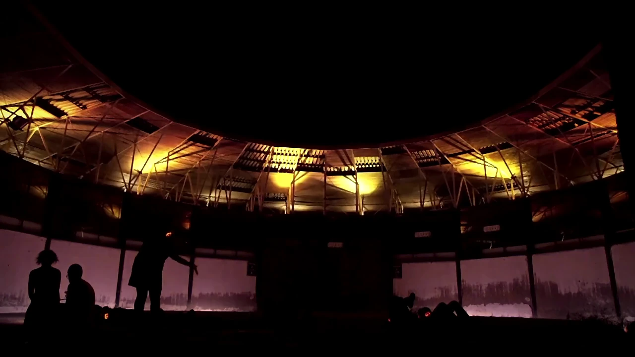 Anfiteatro al atardecer con haces de luz y asistentes con auriculares