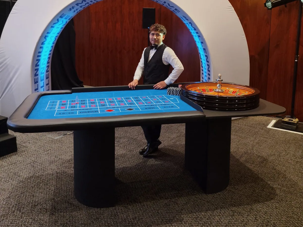 Mesa real de ruleta con tapete azul, rueda de madera y crupier.