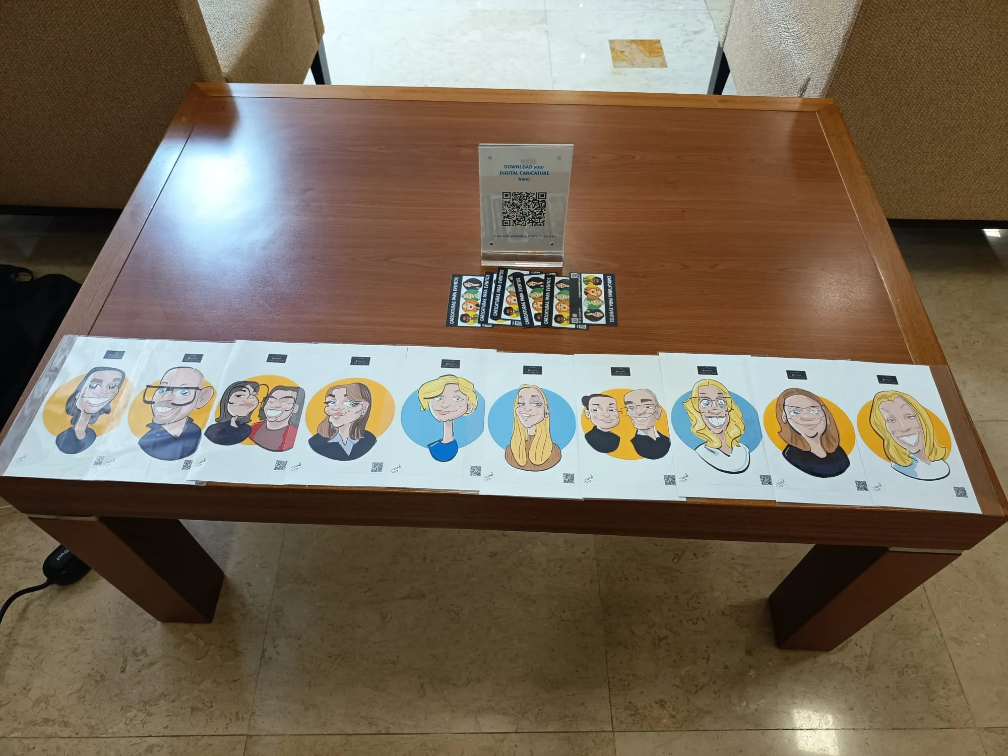 Caricaturas impresas en 10 × 15 cm sobre la mesa del evento, con QR de descarga