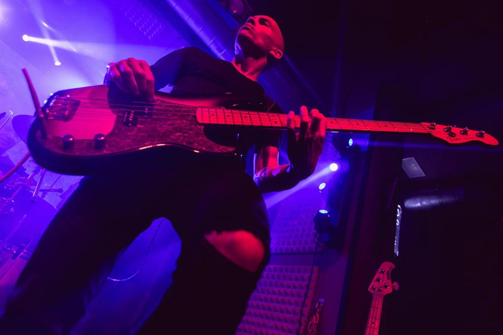 Bajista en contrapicado tocando un bajo eléctrico bajo luces azules y magentas en un escenario oscuro