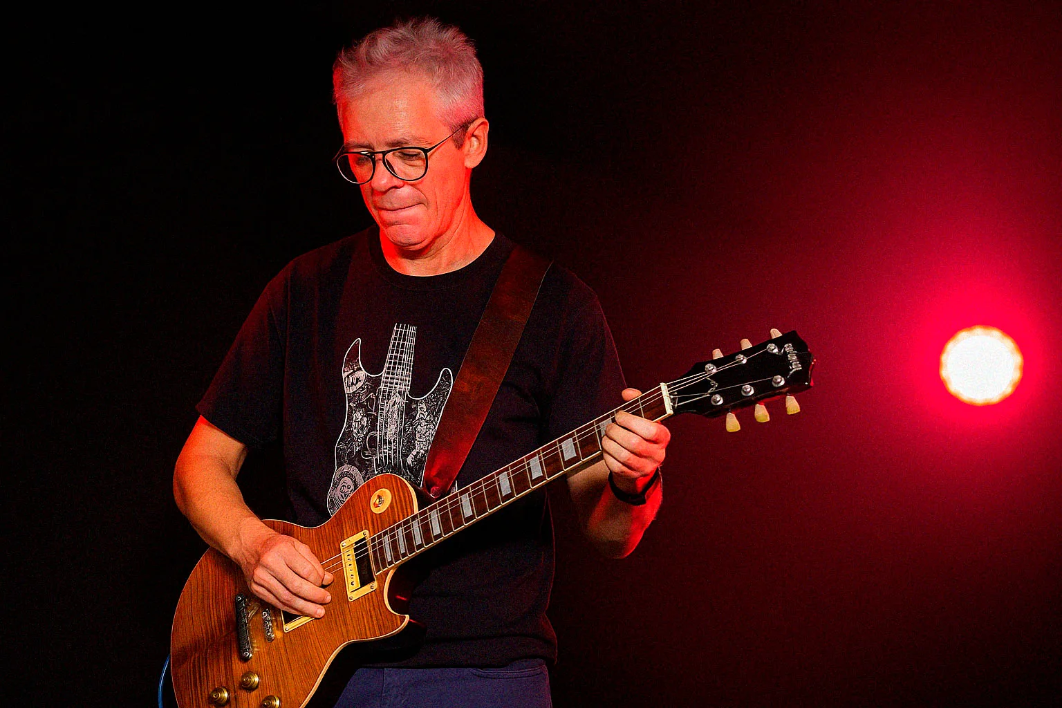 Guitarrista con guitarra eléctrica de cuerpo macizo bajo un foco rojo