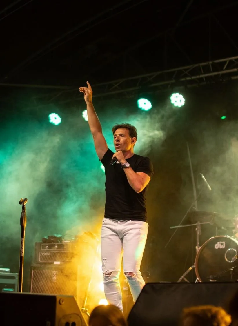 Cantante señalando al cielo en un escenario con humo verde y focos