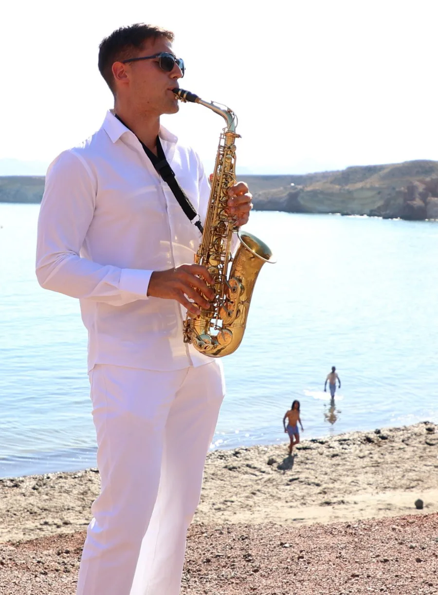 Saxofonista con traje blanco tocando junto a la orilla del mar.